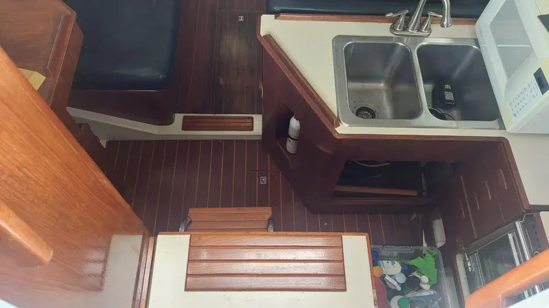 Slide: The Image of 1987 Hunter 34 yacht interior with wooden flooring, dual sink, and compact kitchen area. - 15