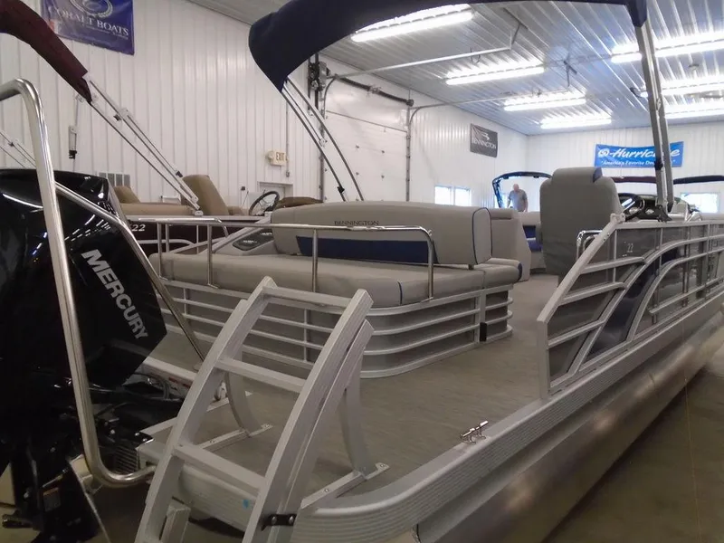 Slide: The Image of 2023 Bennington 22 LSB pontoon boat in showroom, featuring Mercury outboard motor. - 17