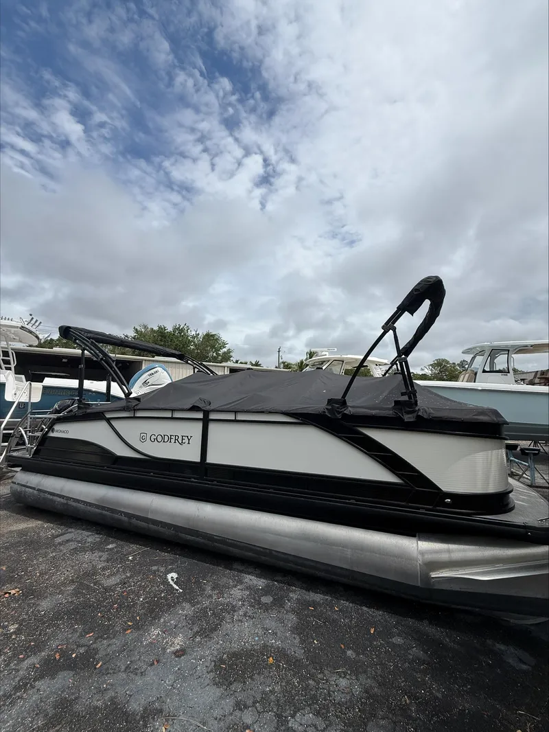 Slide: The Image of 2023 MONACO 235 DFL pontoon boat with cover, parked outdoors under cloudy sky. - 3