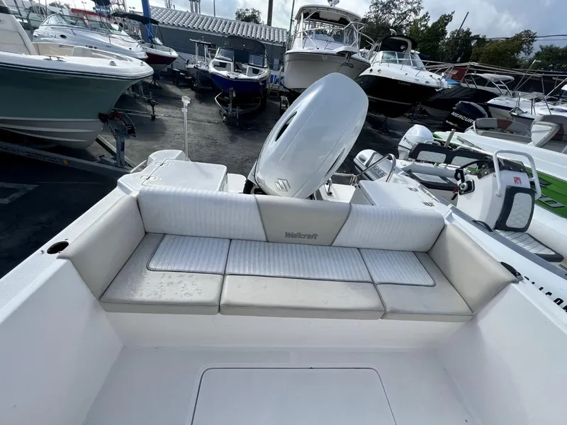 Slide: The Image of 2022 Wellcraft 220CC boat with cushioned seating and outboard motor in a marina. - 26