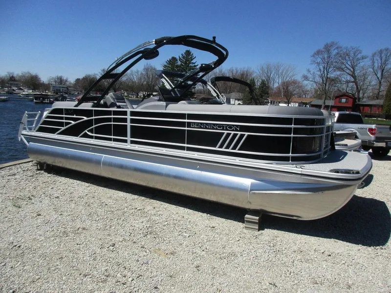 Slide: The Image of 2023 Bennington 24 LXFBA pontoon boat docked on gravel near a lake. - 3