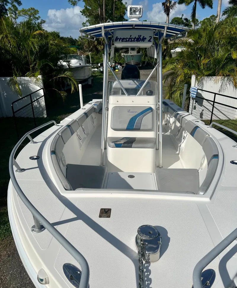 Slide: The Image of 2016 Renegade 250 boat with white deck and blue accents, docked near lush greenery. - 15