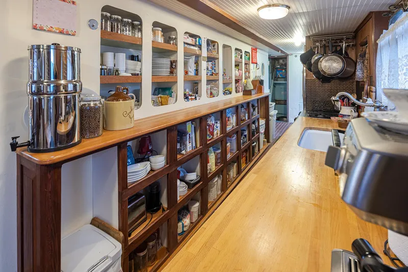 Slide: The Image of Galley kitchen in a 1943 custom Navy tugboat, featuring wooden shelves and modern appliances. - 18