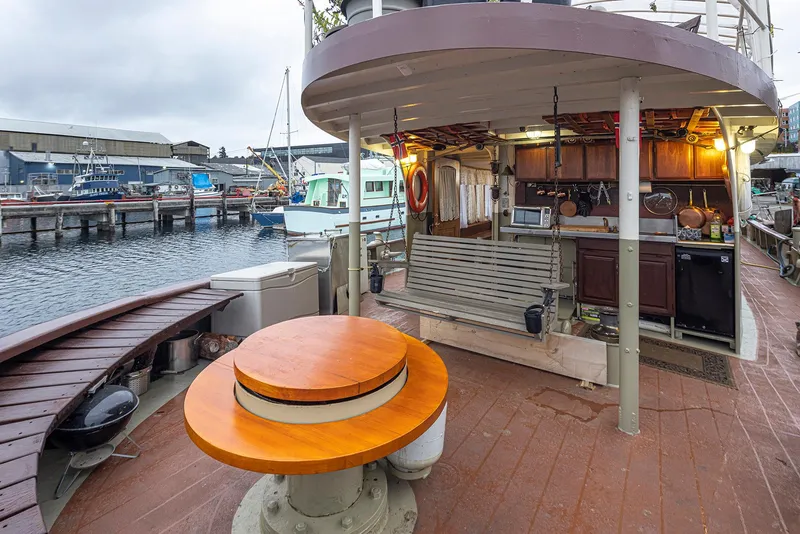 Slide: The Image of 1943 Custom Navy Tugboat with outdoor seating and kitchenette, docked at a marina. - 8
