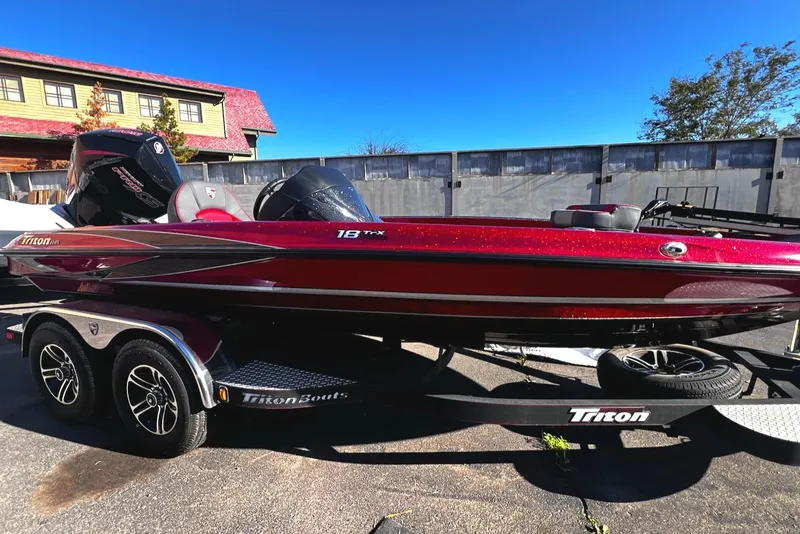 Slide: The Image of 2023 Triton 18 TrX bass boat on trailer, red and black, parked outdoors. - 4