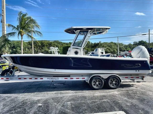Slide: The Image of 2023 Robalo 266 Cayman boat on a trailer, parked outdoors. - 2