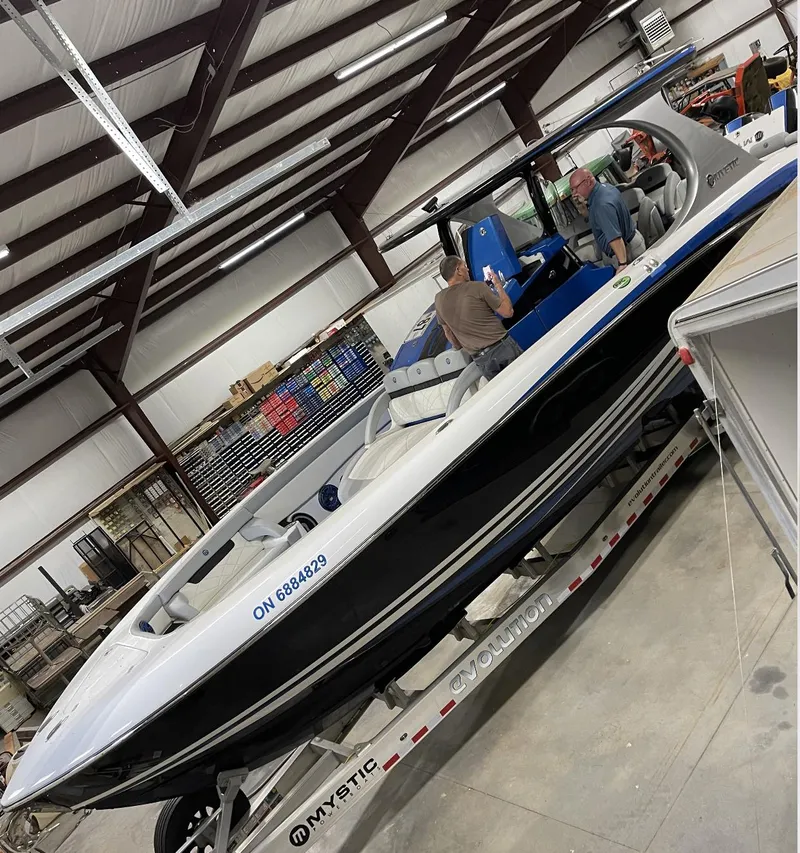 Slide: The Image of 2020 Mystic 3800 boat in a warehouse, on a trailer, with people inspecting it. - 7