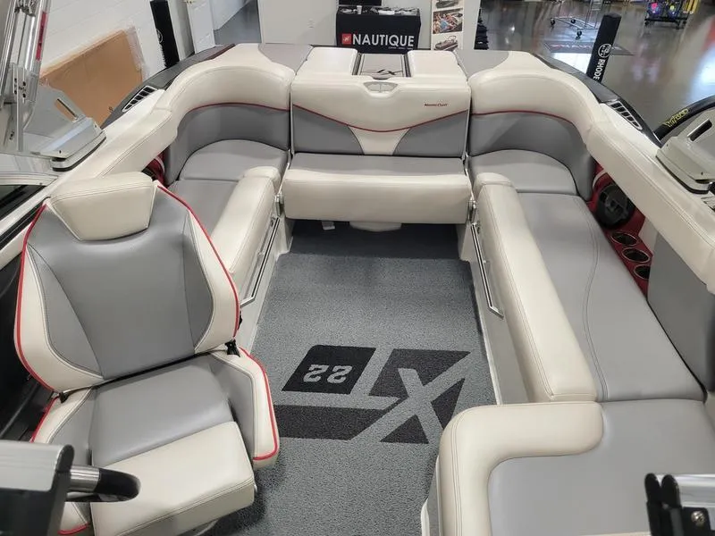 Slide: The Image of 2018 MasterCraft XT22 boat interior with gray and white seating, red accents, and branded carpet. - 12