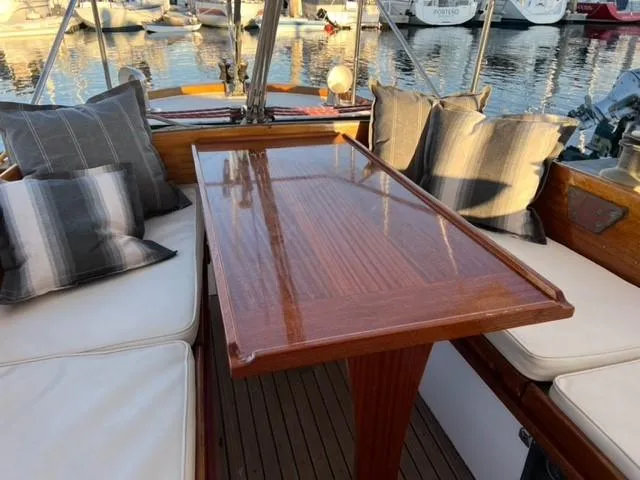 Slide: The Image of Cozy seating area on a 1961 Lapworth 40 yacht with polished wooden table and cushions. - 9