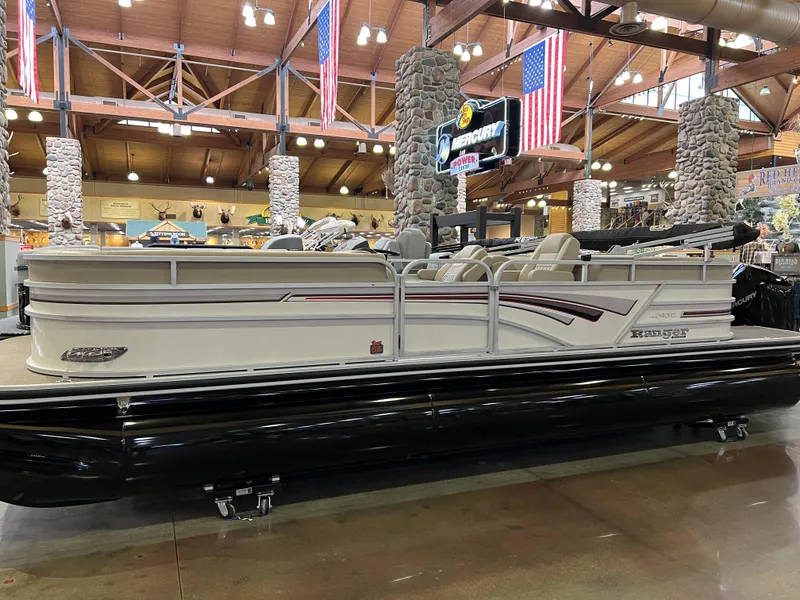 Slide: The Image of 2023 Ranger Reata 243C pontoon boat displayed indoors with American flags. - 2