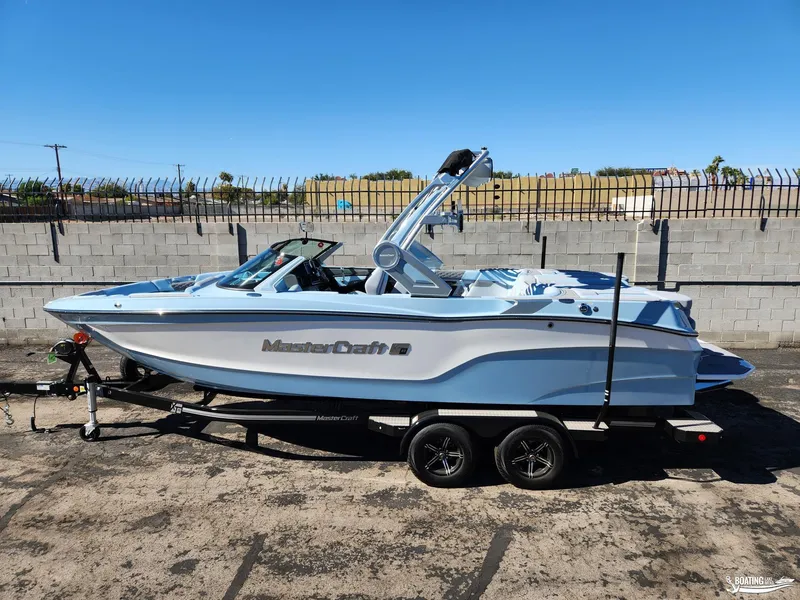 Slide: The Image of 2023 MasterCraft XT23 boat on trailer, light blue and white, parked outdoors. - 0