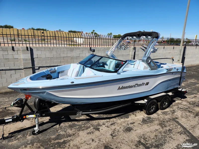 Slide: The Image of 2023 MasterCraft XT23 boat on trailer, parked outdoors, clear sky background. - 1