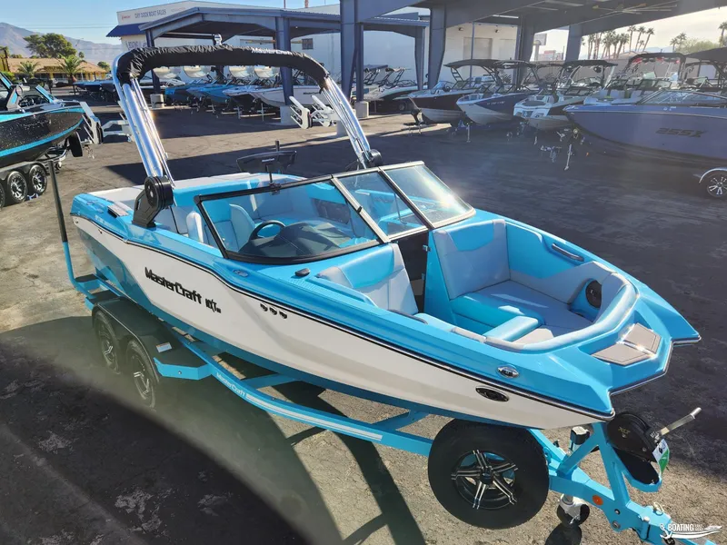 Slide: The Image of 2023 MasterCraft NXT20 boat in vibrant blue and white, displayed on a trailer at a dealership. - 2
