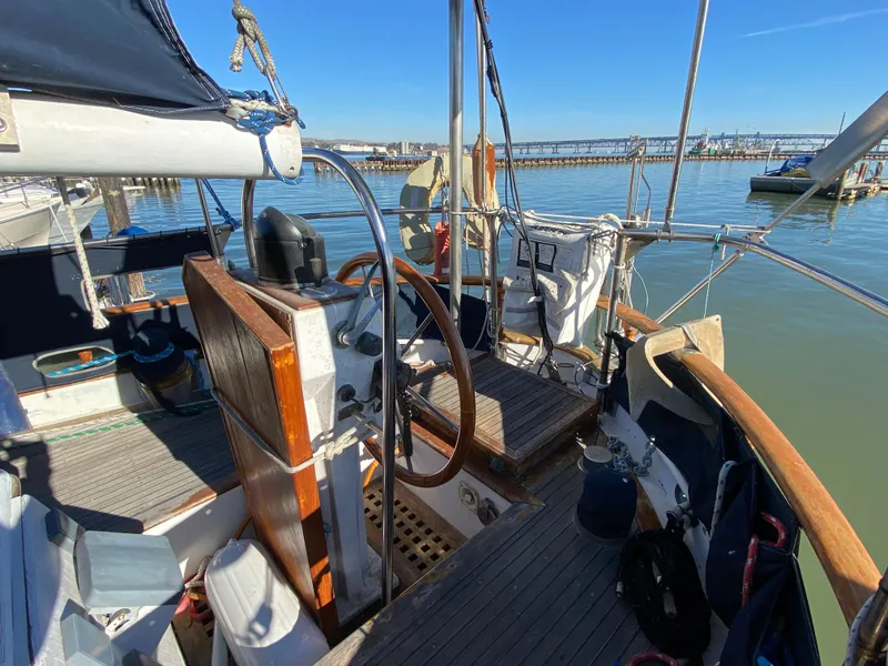 Slide: The Image of 1979 CT 48 sailboat cockpit with wooden wheel, docked in a marina under clear blue skies. - 7