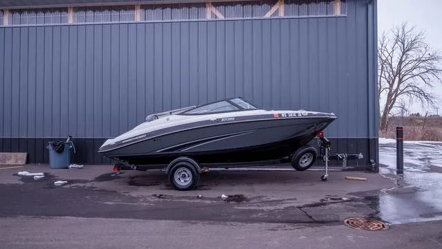Slide: The Image of A 2014 Yamaha SX192 boat on a trailer in front of a gray building. - 2