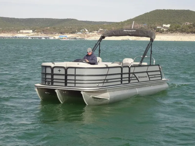 Slide: The Image of 2023 Berkshire 24UL CTS 3.0 pontoon boat cruising on a lake with scenic hills. - 4