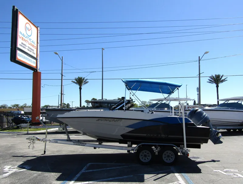 Slide: The Image of 2023 Starcraft SVX 190 OB boat on trailer with blue canopy in parking lot. - 1