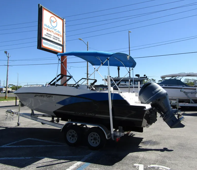 Slide: The Image of 2023 Starcraft SVX 190 OB boat with blue canopy on trailer at dealership. - 2