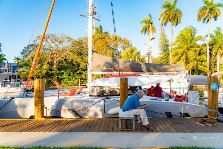 Slide: The Image of 2024 Excess 11 catamaran docked with people on board, surrounded by palm trees. - 2