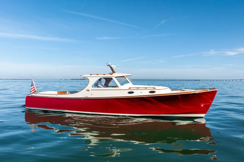 Slide: The Image of 1996 Hinckley 36 Picnic Boat Classic on calm water, featuring a sleek red hull. - 2