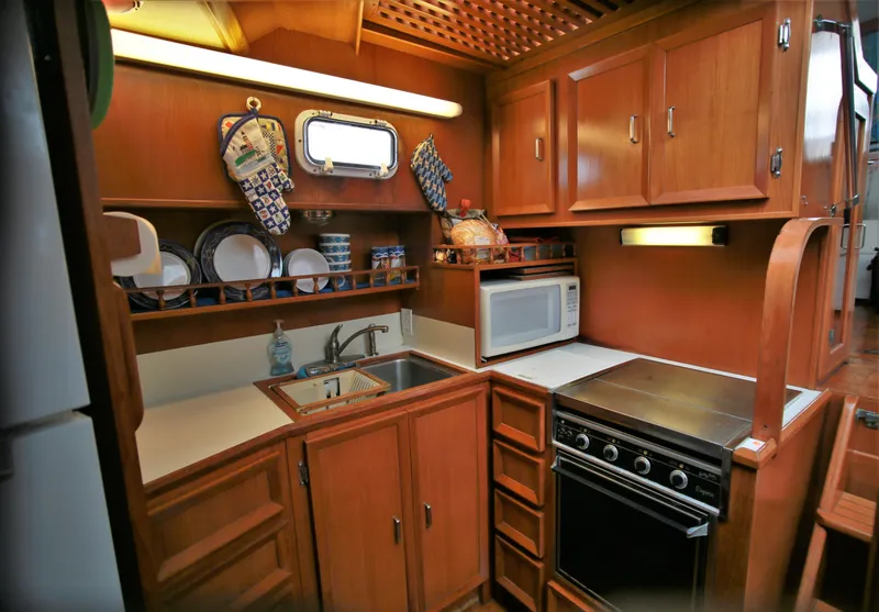 Slide: The Image of 1987 Jefferson 42 Sundeck Motor Yacht kitchen with stove, microwave, and wooden cabinetry. - 33