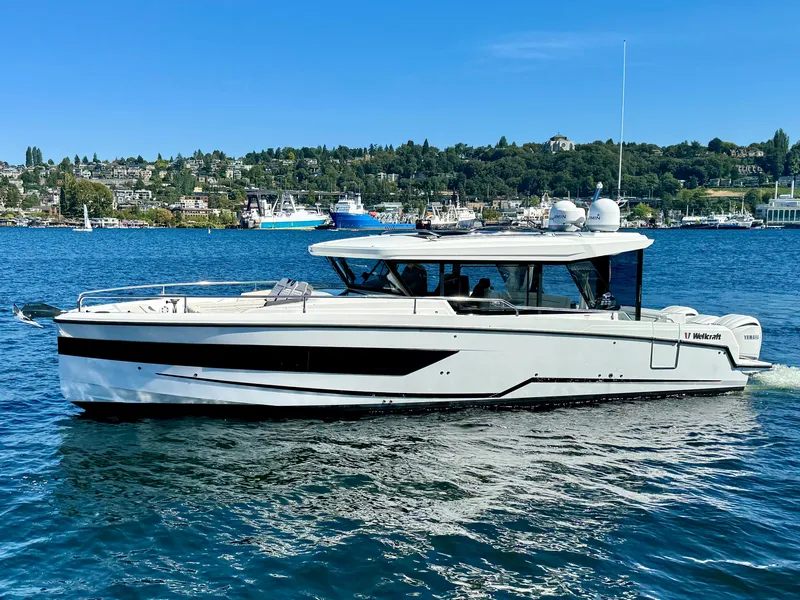 Slide: The Image of 2024 Wellcraft 355 boat cruising on a scenic lake with lush green shoreline. - 10