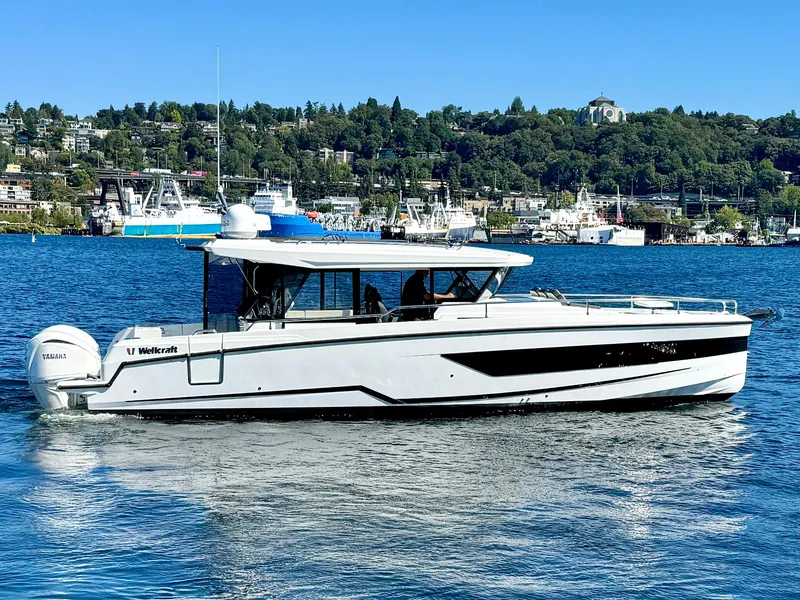 Slide: The Image of 2024 Wellcraft 355 boat cruising on a scenic lake with a city backdrop. - 5