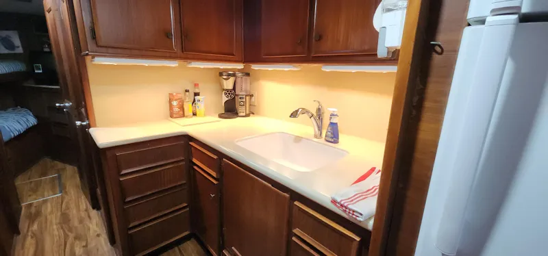 Slide: The Image of 1978 Hatteras Sportfish kitchen with wooden cabinets, sink, and countertop appliances. - 26