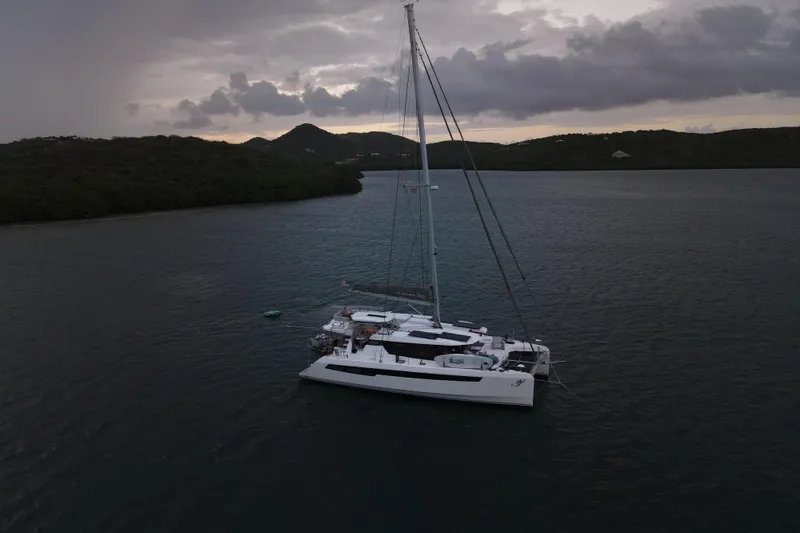 Slide: The Image of Sailing catamaran Leopard 50, 2023 model, anchored in a serene bay at dusk. - 2