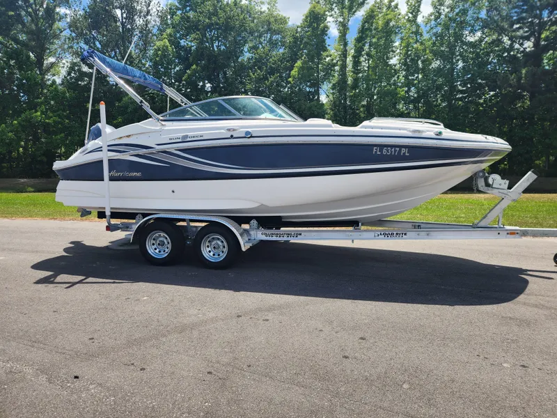 Slide: The Image of 2013 Hurricane SunDeck 2200 OB boat on a trailer, parked on a sunny day. - 0