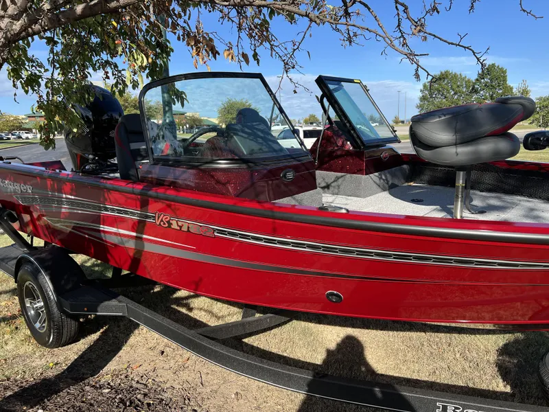 Slide: The Image of 2023 Ranger VS1782SC Angler boat in red, parked on a trailer under a tree. - 2