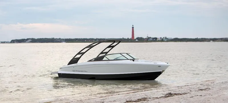 Slide: The Image of 2025 Regal LS2 boat on calm water near a sandy shore with a distant lighthouse. - 0