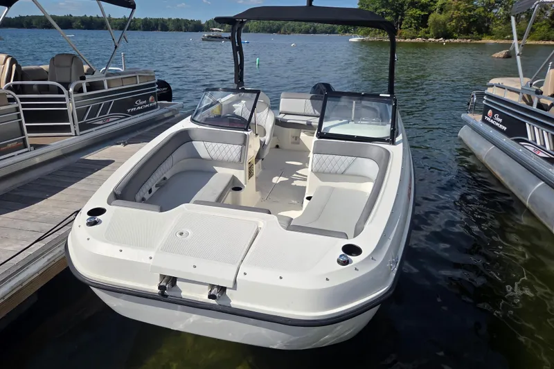 Slide: The Image of 2023 Bayliner DX 2200 boat docked on a serene lake with clear skies. - 2