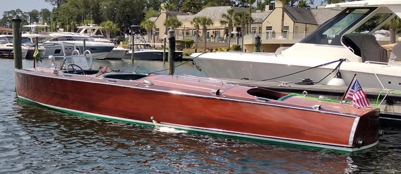Slide: The Image of 1988 Hacker-Craft 30 Triple Cockpit boat docked, featuring classic wooden design and American flag. - 21