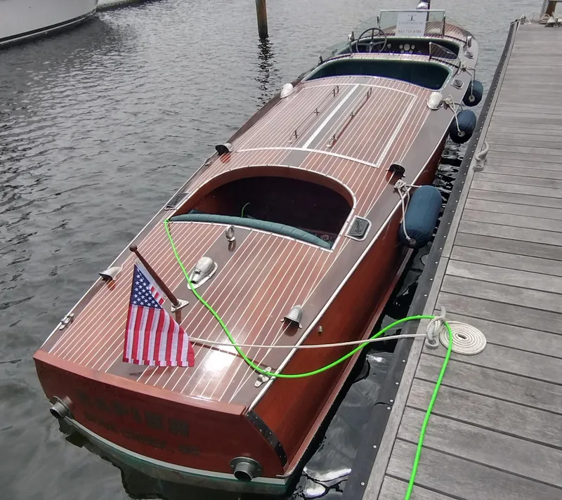 Slide: The Image of 1988 Hacker-Craft 30 Triple Cockpit boat docked, featuring classic wooden design and American flag. - 23
