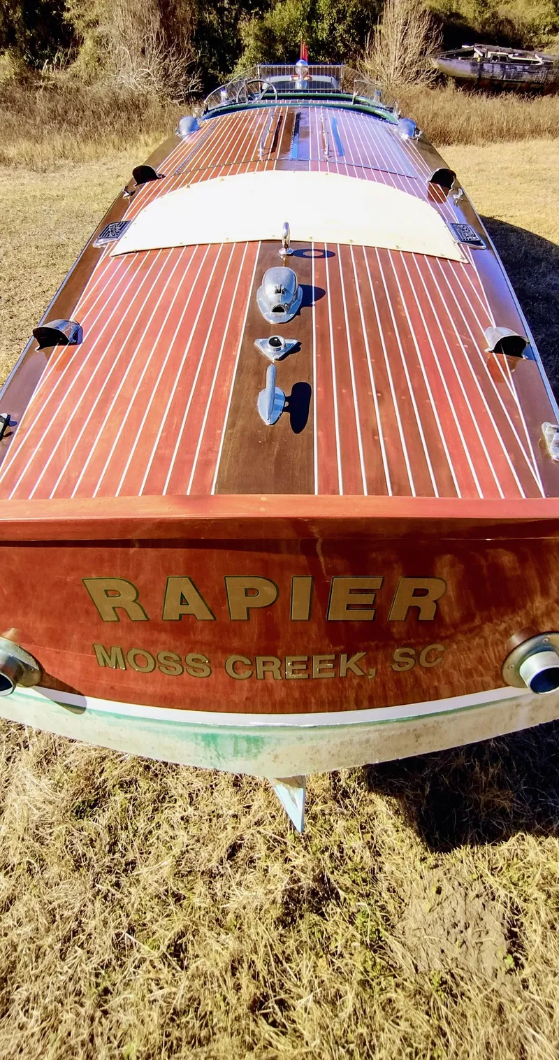 Slide: The Image of 1988 Hacker-Craft 30 Triple Cockpit boat with wooden finish, labeled "RAPIER," on grassy terrain. - 4