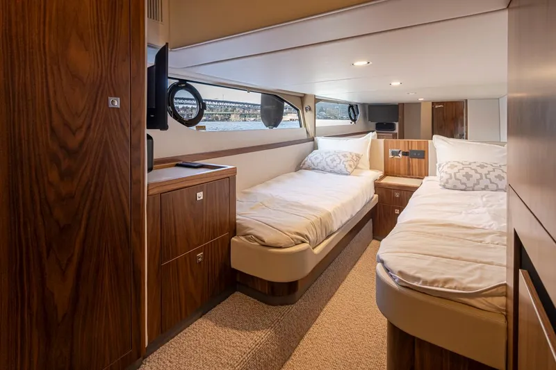 Slide: The Image of 2024 Riviera 46 Sports Motor Yacht cabin with twin beds and wooden interior. - 17