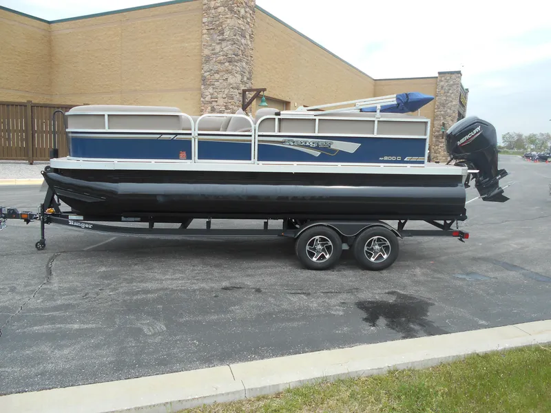 Slide: The Image of 2023 Ranger Reata 200C pontoon boat on a trailer in a parking lot. - 2