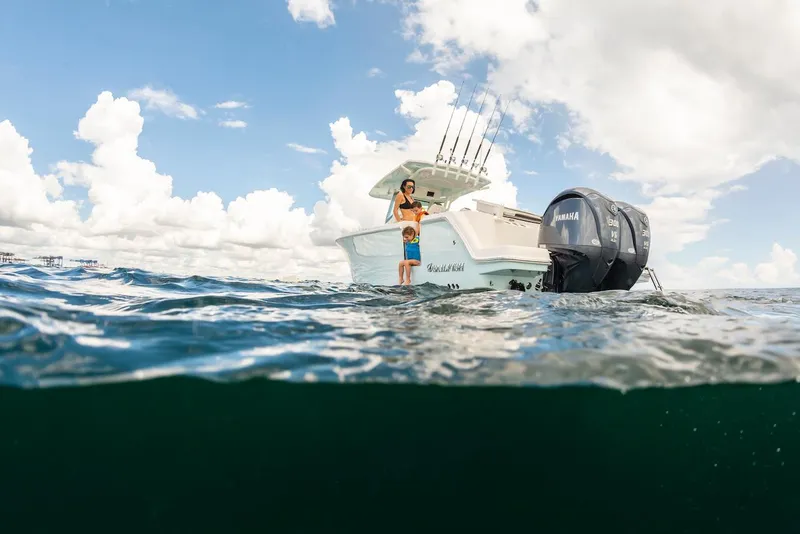 Slide: The Image of 2024 Sailfish 312 CC boat on water, with person standing, under cloudy sky. - 11