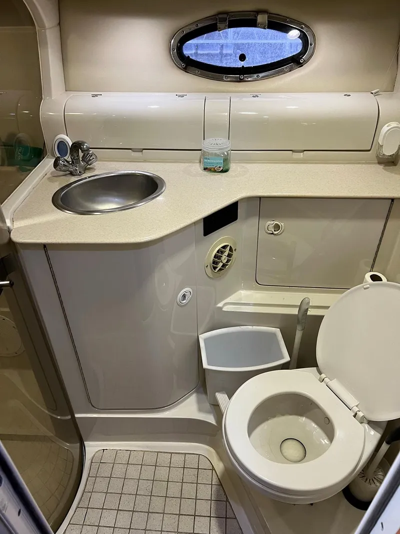 Slide: The Image of Compact bathroom in a 1999 Regal 402 boat, featuring a sink, toilet, and porthole window. - 38