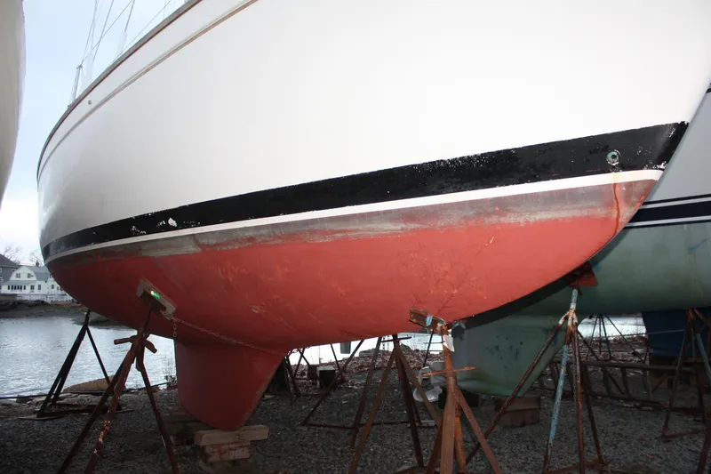 Slide: The Image of 1979 Pearson 323 sailboat hull on stands, red bottom paint, black stripe, dockside. - 4