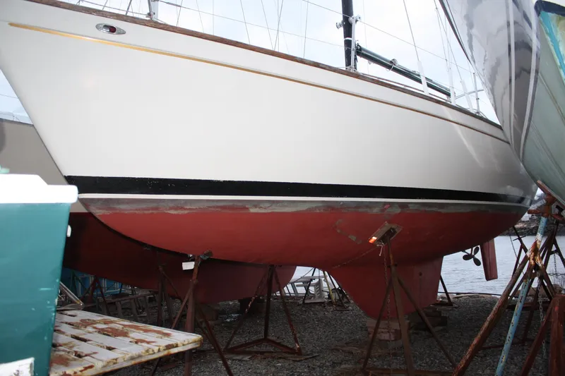 Slide: The Image of 1979 Pearson 323 sailboat on stands, white hull with red bottom, dockside view. - 5