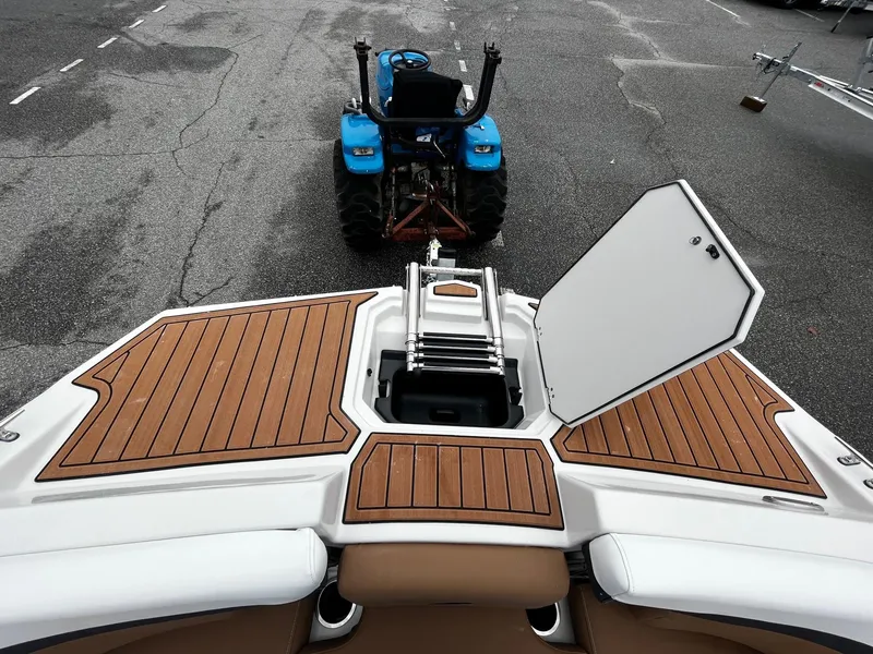 Slide: The Image of 2024 Starcraft SVX 231 boat with open storage compartment, wooden deck, and blue tractor in background. - 21