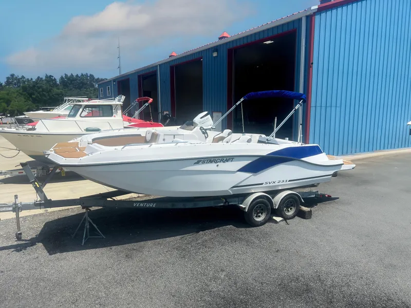 Slide: The Image of 2023 Starcraft SVX 231 OB DH boat on trailer near blue warehouse. - 0