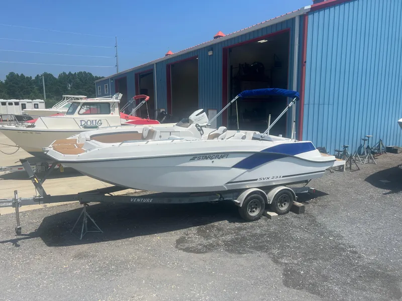 Slide: The Image of 2023 Starcraft SVX 231 OB DH boat on trailer near blue building. - 3