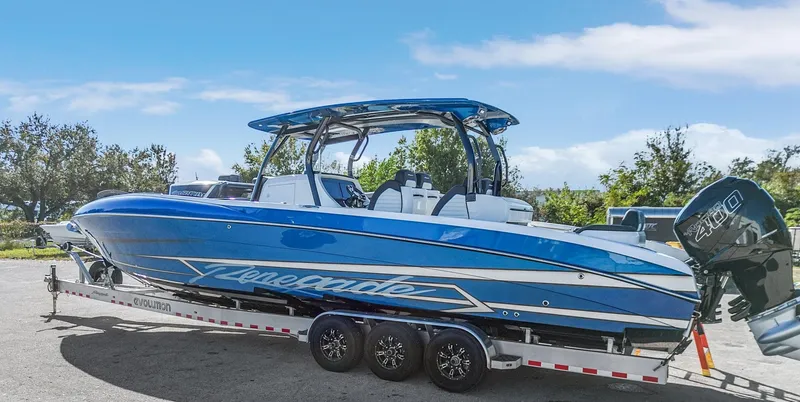 Slide: The Image of 2023 Renegade 38 Open boat on trailer, blue and white design, parked outdoors. - 45
