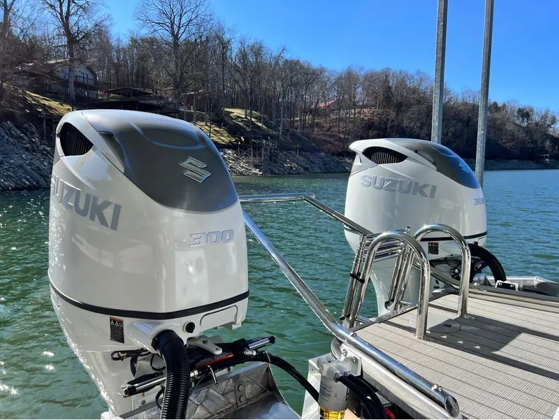 Slide: The Image of Twin Suzuki 300 outboard motors on a 2023 Manitou LX 25 SRW boat by a lake. - 14