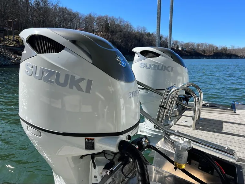 Slide: The Image of Twin Suzuki outboard motors on a 2023 Manitou LX 25 SRW boat by a lake. - 33