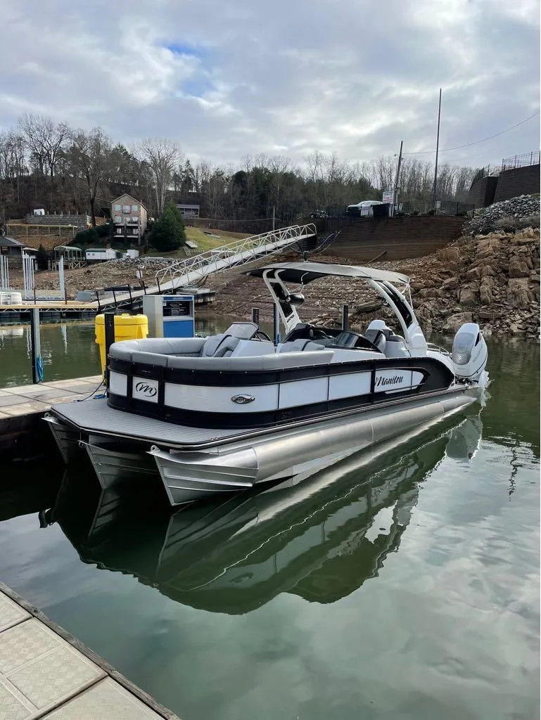Slide: The Image of 2023 Manitou LX 25 SRW pontoon boat docked on a calm lake. - 44