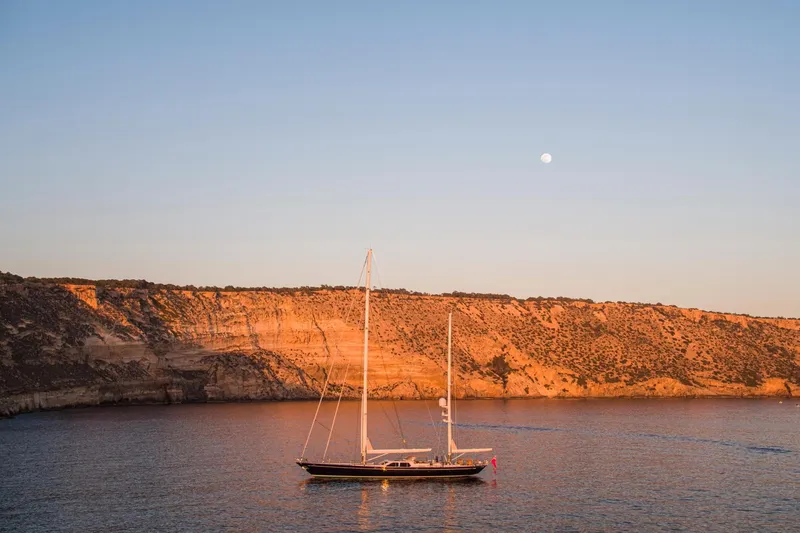 Slide: The Image of Alloy Yachts Cruising Ketch 1998 near rocky coastline at sunset. - 49